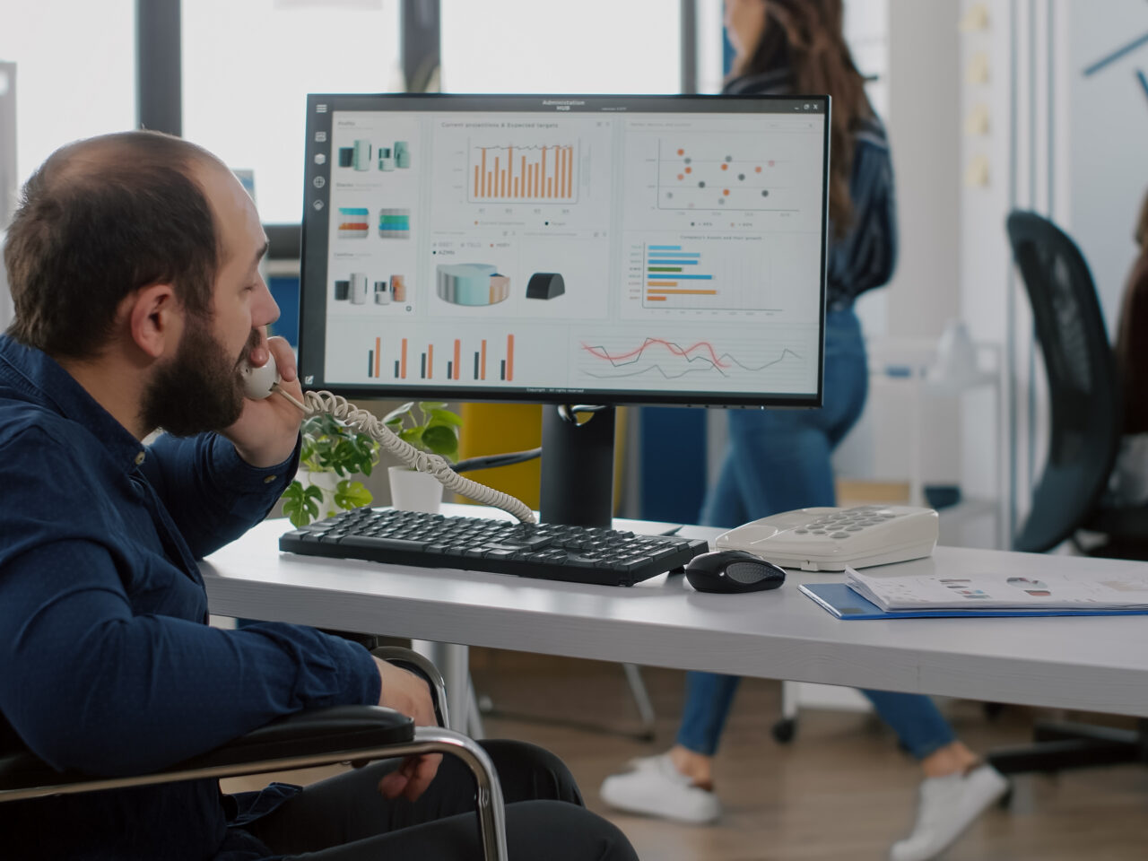 Busy paralysed handicapped team leader answering phone talking with partner typing on computer explaning project ideea and checking financial data. Diverse colleagues working in start up office