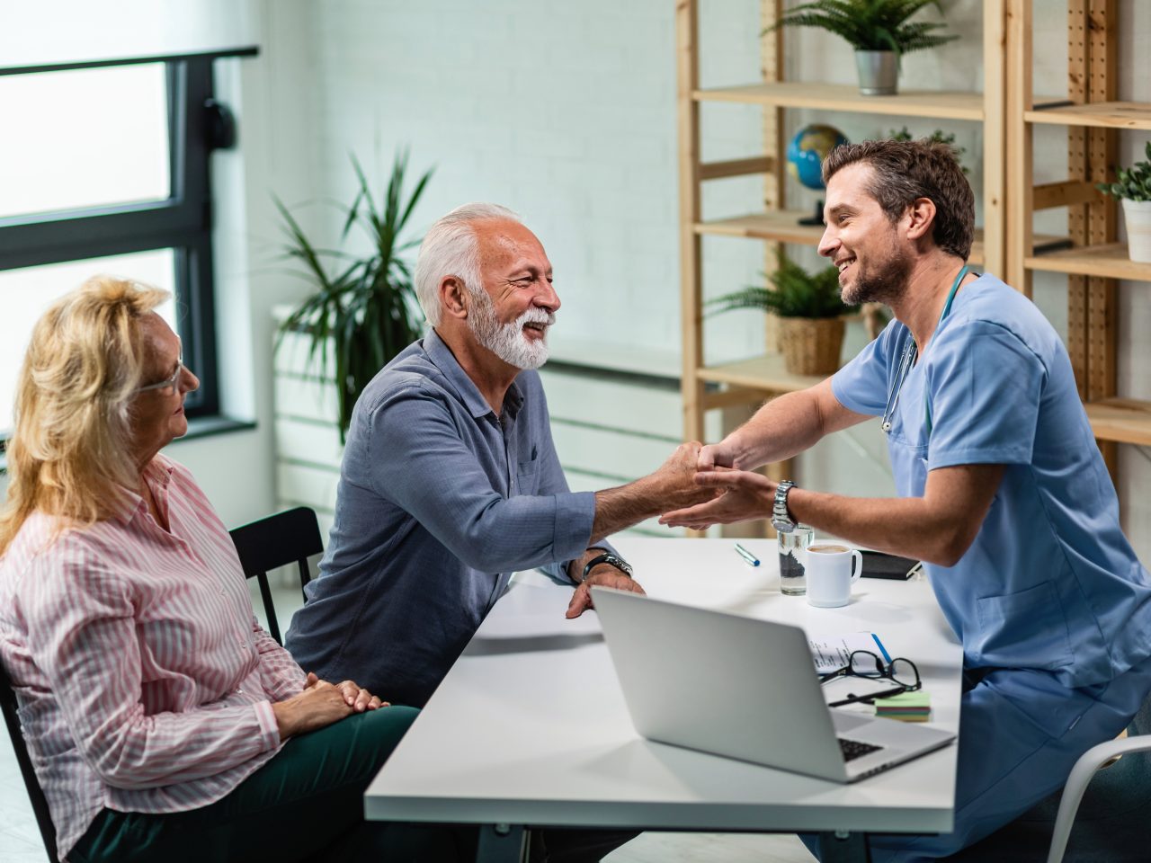 Happy male doctor shaking hands with senior man who came to medical appointment with his wife.
