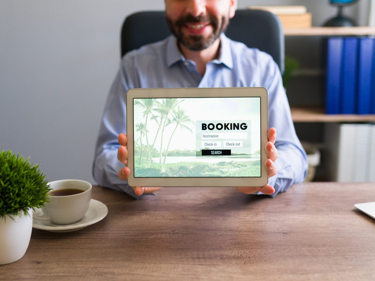 Happy travel agent smiling while holding a tablet screen with a booking trip. Sales representative showing travel information to a customer at his office