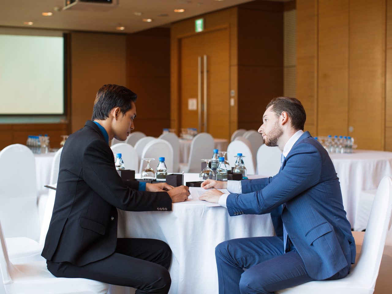 Two serious adult business men sitting at table, working with documents and discussing issue in conference room