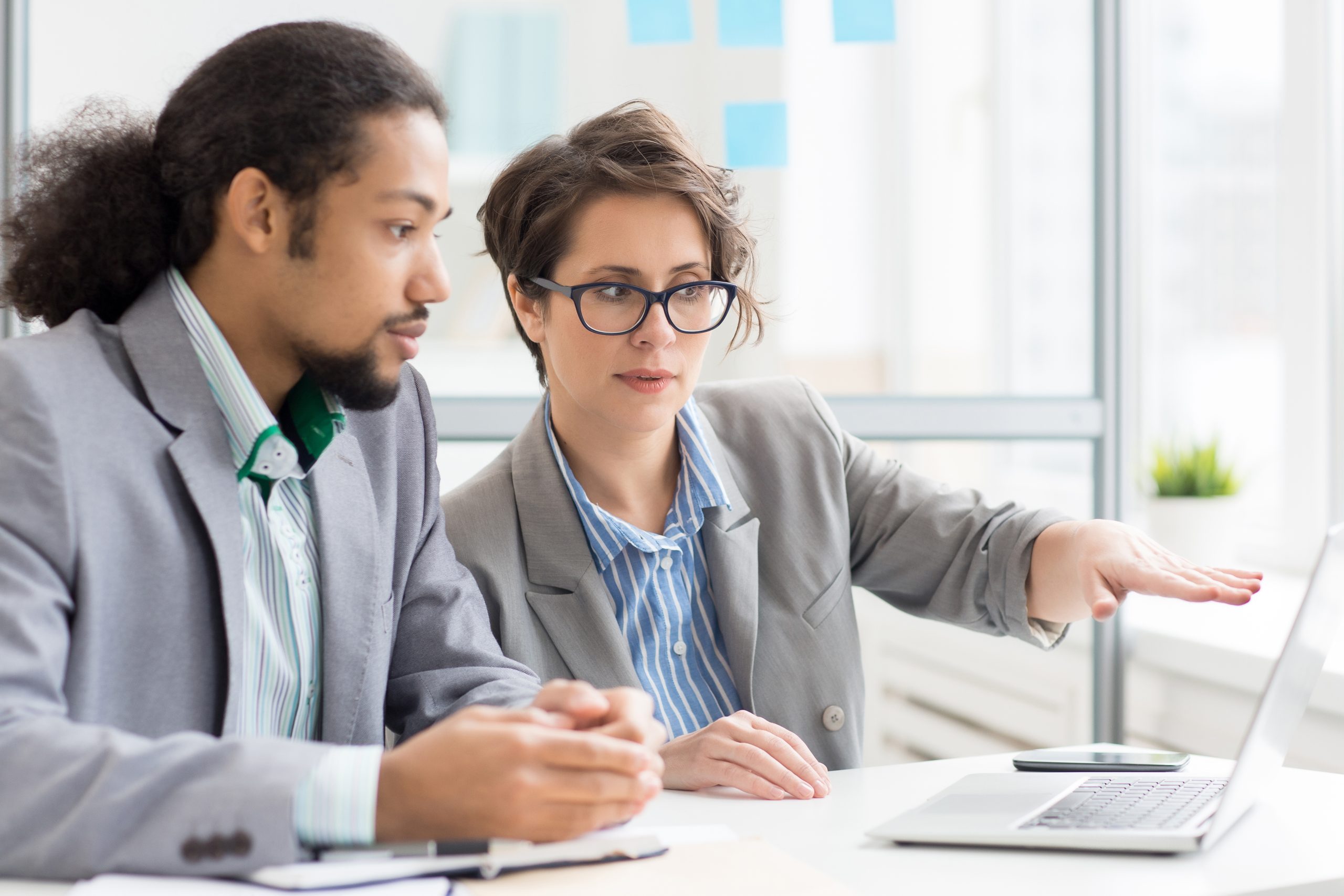 Young manager pointing at online data in laptop while discussing it with colleague